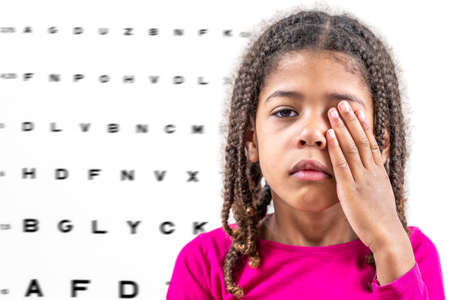Child girl closing eye, showing size or sign from eye chart, vision diagnostics.の写真素材