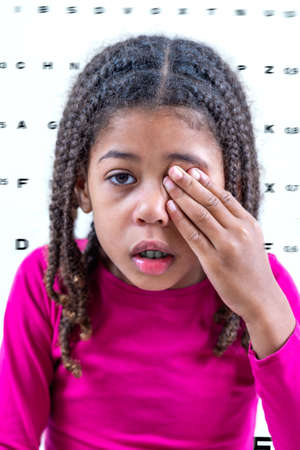 Child girl closing eye, showing size or sign from eye chart, vision diagnostics.の写真素材