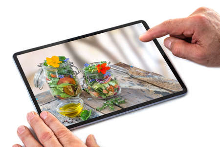 Man hands scrolling screen of tablet computer for food photo of vegetables salad with tomatoes and...
