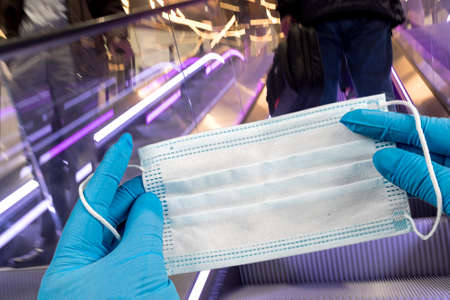 .Hand holding mask and wearing for protection from virus or air pollution on supermarket stairs backgroundの写真素材