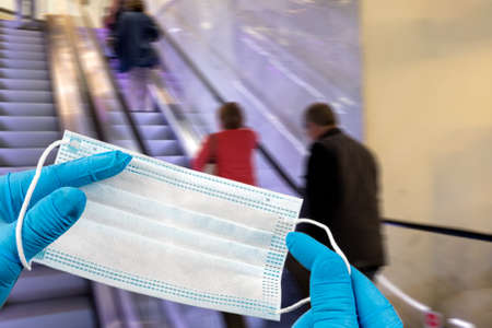 .Hand holding mask and wearing for protection from virus or air pollution on supermarket stairs backgroundの写真素材