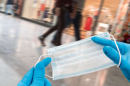 .Hand holding mask and wearing for protection from virus or air pollution on supermarket stairs backgroundの写真素材