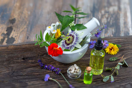 Herbs in mortar with pestle and organic essential aroma oil in glass bottle isolated on rustic...