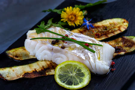 Cod back with zucchini on black dishの写真素材