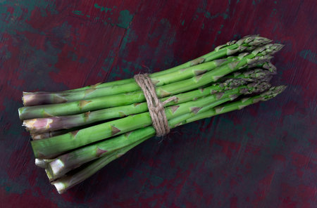Close-up of a fresh raw asparagus bunch tied with a burlap twine isolated old wooden background.の写真素材
