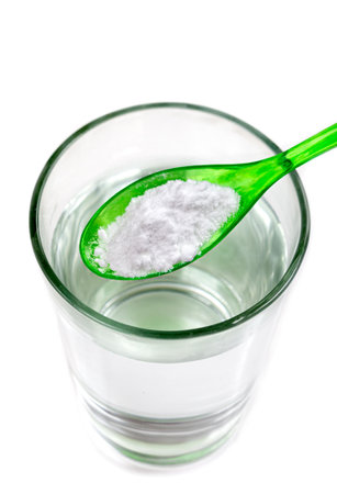 Spoon of baking soda over glass of water, isolated on white backgrpndの写真素材