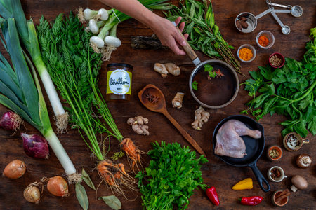 Chicken broth with pieces chicken and vegetables in a metal casserole and in a soup cup on dark wooden table, view from above, close-upの写真素材