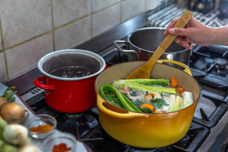 womanman mixes the delicious and fragrant broth in a pot on the gas stove in the kitchenの写真素材