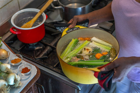womanman mixes the delicious and fragrant broth in a pot on the gas stove in the kitchenの写真素材