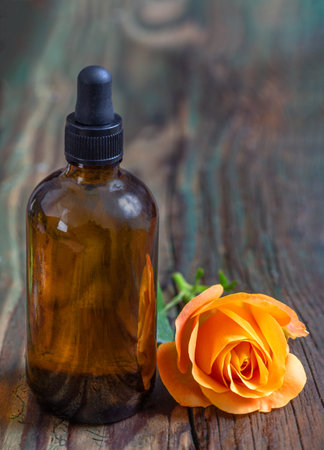 Romantic aromatherapy. Pink fresh blossom rose essential oil in dark glass bottle. wooden bacgroundの写真素材