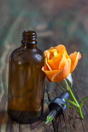 Romantic aromatherapy. Pink fresh blossom , rose essential oil in dark glass bottle. wooden bacgroundの写真素材