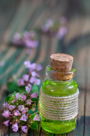 Essential oil of oregano in a bottle and fresh flowers on a wooden table Natural cosmetics and aromatherapyの写真素材