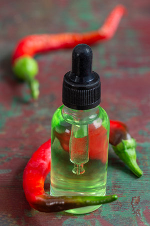 A glass bottle of essential oil with fresh red and green chili on wooden backgroundの写真素材