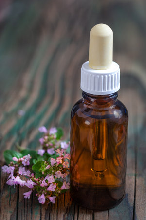 Essential oil of oregano in a bottle and fresh flowers on a wooden table Natural cosmetics and aromatherapyの写真素材