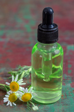 Small glass bottle with essential roman chamomile oil on the old wooden background. Chamomile flowers, close up. Aromatherapy, spa and herbal medicine ingredients. .の写真素材