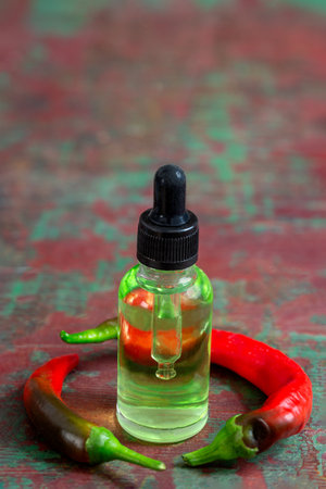 A glass bottle of essential oil with fresh red and green chili on wooden backgroundの写真素材