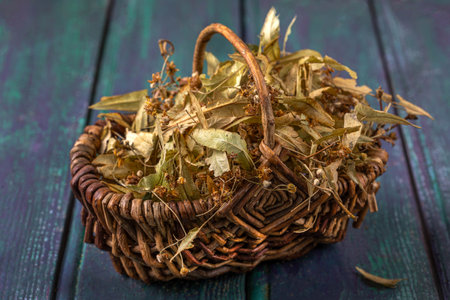 Dried herbs in a woven basket on a wooden surfaceの写真素材