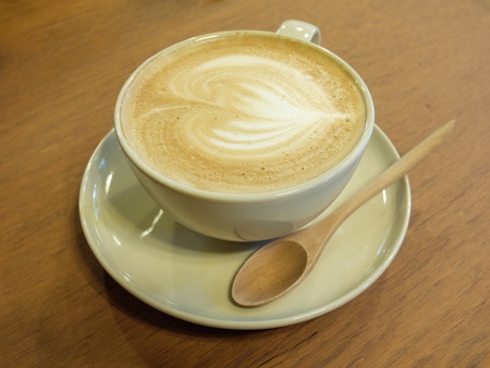A cup of coffee with heart pattern in a white cup on wooden backgroundの写真素材