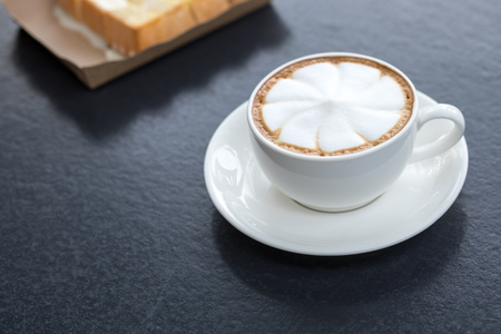 Hot art latte coffee in cup on black table with toastの写真素材