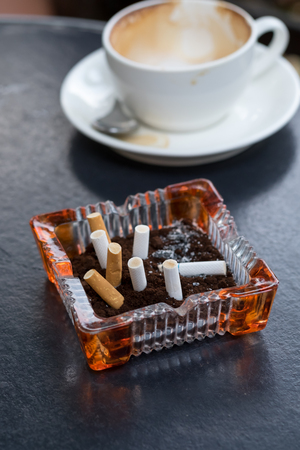Empty coffee cup after drink with cigarette butt on wood tableの写真素材