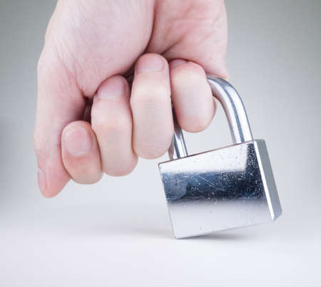 Little finger holding the used, scratchy, silver padlock isolated on whiteの写真素材