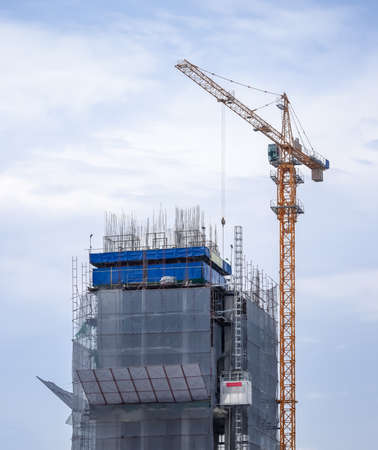 Under construction high building showing its structure with tall crane isolated on cloudy sky