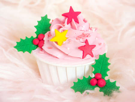 Sweet pink cupcake with stars and holly berry decorated on soft fur backgroundの写真素材