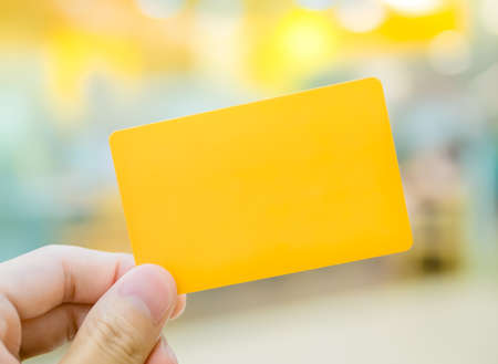Hand holding yellow dummy card (to be replaced with your own) in the elegance atmosphereの写真素材