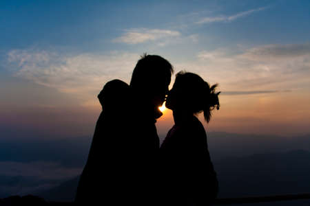 silhouette of couple kissing with sunrise in winter on mountainの写真素材