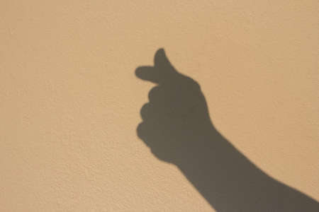 shadow of mini heart hand sign on brown wallの写真素材