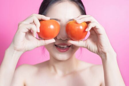 Asian woman with tomato concept. She smiling and holding tomato. Beauty face and natural makeup. Isolated over pink backgroundの写真素材