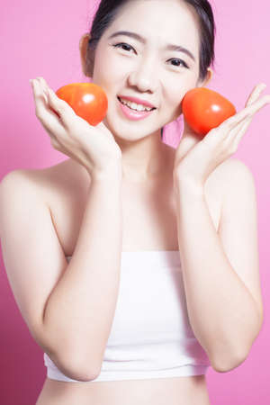 Asian woman with tomato concept. She smiling and holding tomato. Beauty face and natural makeup. Isolated over pink backgroundの写真素材