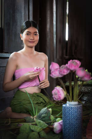 Beautiful Thai woman holding pink lotus wearing Thai traditional costume