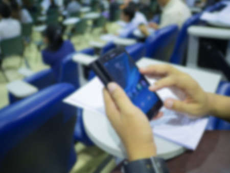 Hand holding smart phone on auditorium room blur backgroundの写真素材