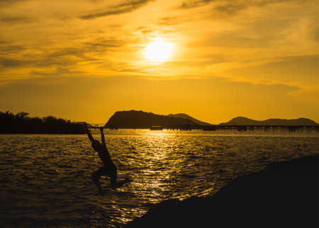 Silhouette man jumping sea over sunset