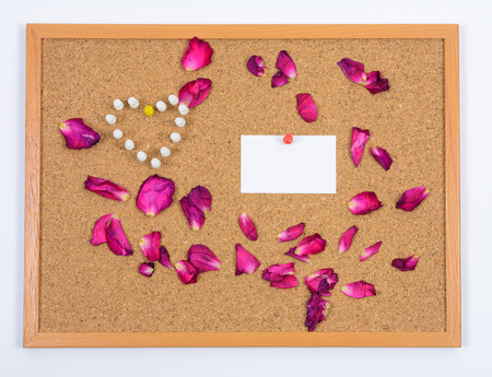 Rose petals, paper card and push pins on brown boardの写真素材