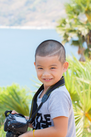 Little smiling boy holding digital camara in gardenの写真素材