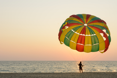 Man hold parachute for tourist on sand beach at sunset timeの写真素材