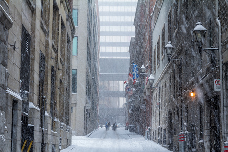 Street of Old-Montreal in winter under a snow storm with a modern skyscraper in the backgroundの写真素材