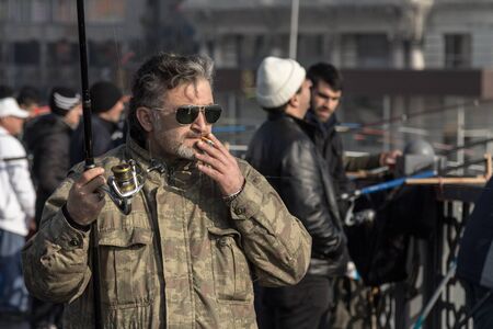 ISTANBUL, TURKEY - DECEMBER 27, 2015: Fisherman on Galata bridge smoking a cigarette before starting to fishのeditorial素材
