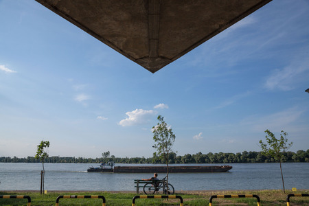 BELGRADE, SERBIA - JUNE 06, 2017: Young man relaxing in front of Danube river, in Belgrade, on Donji Dorcol district, a barge passing by on the waterPicture of a young man relaxing next to his bike in belgrade, capital city of Serbia, with a boat passinのeditorial素材