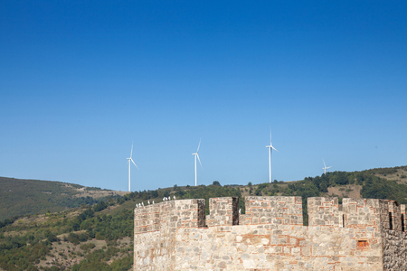 Romanian Wind Farm with Wind Turbine and windmills facing an old castle located on the Serbian side of the Danube river, in the Iron Gates valley.のeditorial素材