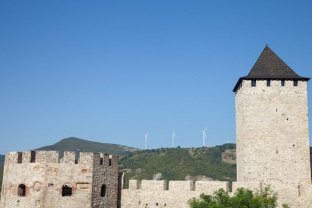 Romanian Wind Farm with Wind Turbine and windmills facing an old castle located on the Serbian side of the Danube river, in the Iron Gates valley.のeditorial素材