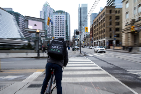 TORONTO, CANADA - DECEMBER 31, 2016: Uber Eats delivery man on a bicycle waiting to cross a street...