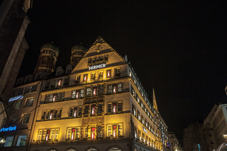MUNICH, GERMANY - DECEMBER 17, 2017: Hirmer department store in a traditional Bavarian building in downtown Munich, Frauenkirche church can be seen in the background. Picture of the Hirmer department shop at night in Munich, Germany, with the Frauenkircのeditorial素材