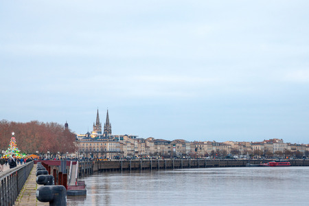 BORDEAUX, FRANCE - DECEMBER 24, 2017: Garonne Quays (Quais de la Garonne) at dusk with a crowd passing by. Saint Andre cathedral can be seen in background.Garonne Quay (Quais de la Garonne), in Bordeaux, France, at dusk, while people are passing by. Theのeditorial素材