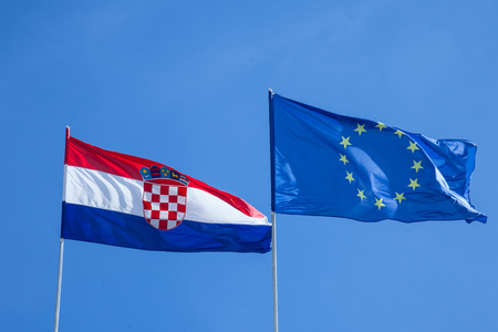 Croatian and European flags waiving in the air with a blue sky background. Croatia is the youngest country that joined the European Union in 2013の写真素材