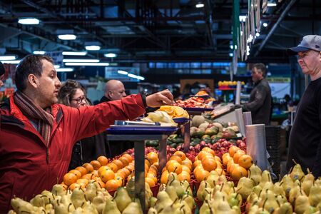 MONTREAL, CANADA - NOVEMBER 3, 2018: Canadian man tasting samples of oranges in Jean Talon Market, in Montreal, Quebec. It is a major landmark & a symbol of Quebec agricultureのeditorial素材