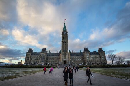OTTAWA, CANADA - NOVEMBER 10, 2018: Tourists standing on front of the center bloc of the Parliament of Canada, with its Main clock tower. in the Canadian Parliamentary complex of Ottawa, Ontarioのeditorial素材