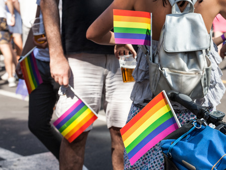 Two men and a woman holding rainbow gay flags in their pockets during a Gay Pride.